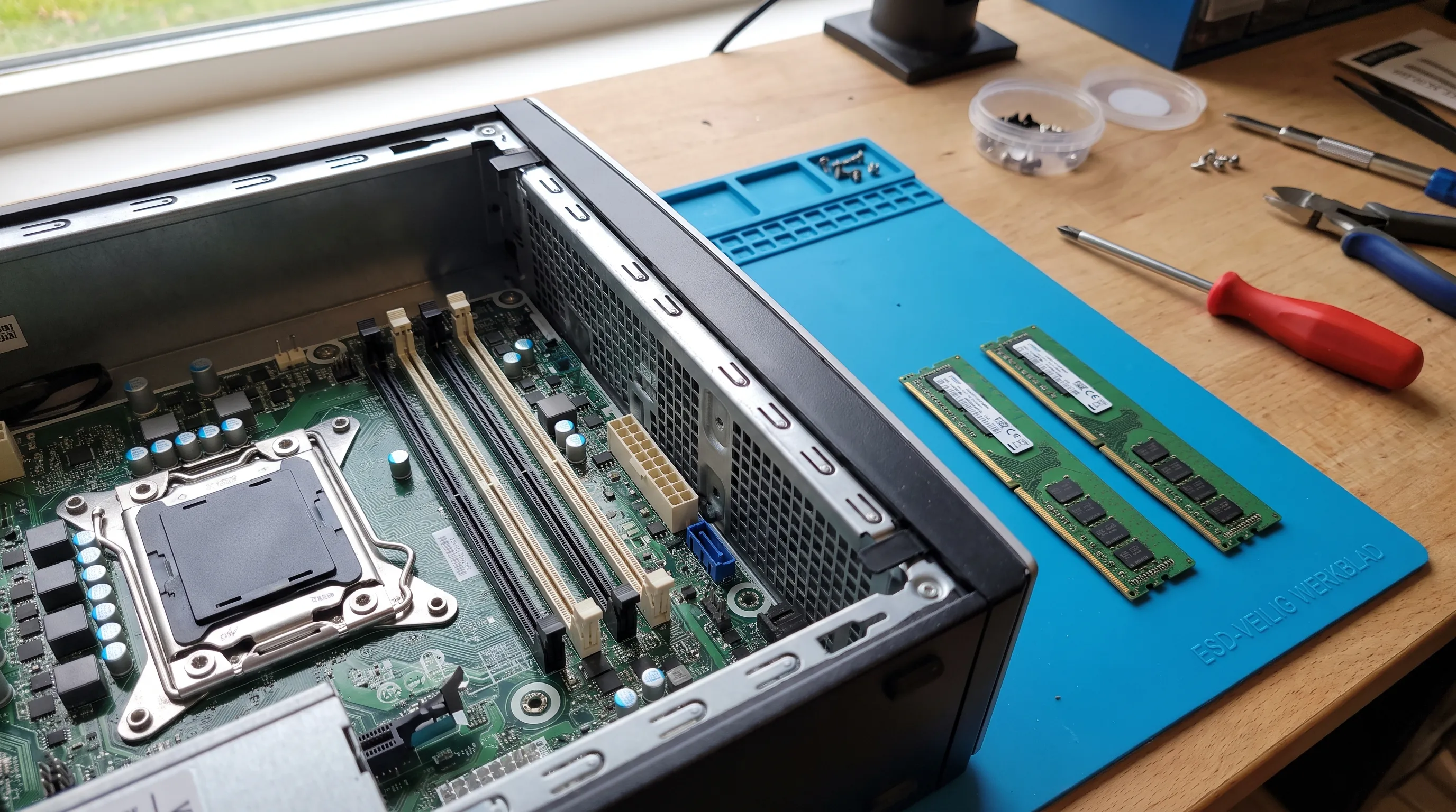 Een open desktop op een werkbank toont lege RAM-sleuven en twee passende modules die klaar liggen voor uitbreiding van het geheugen.