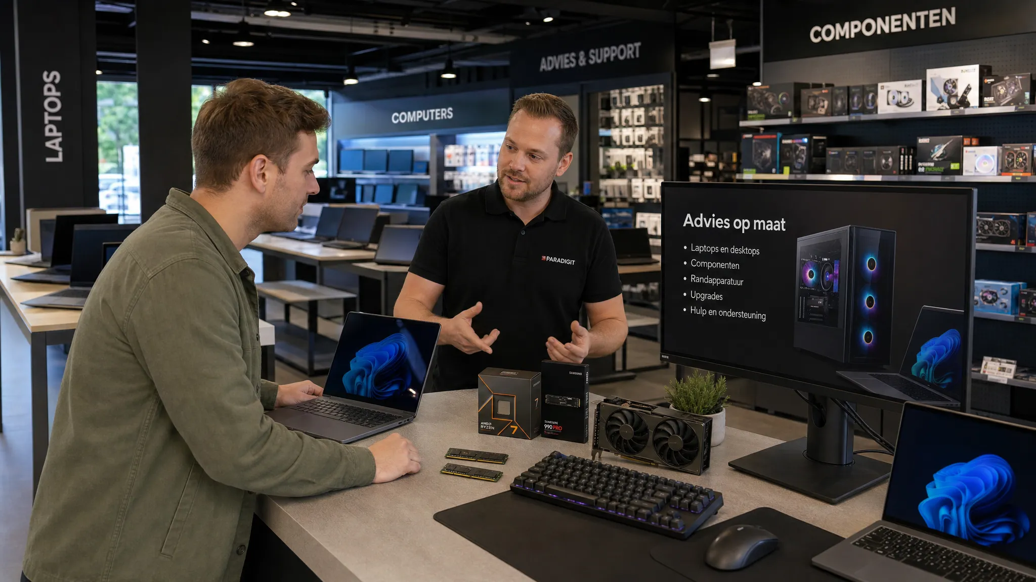 Een klant bespreekt laptop- en desktopopties met een adviseur in een pc winkel, met monitoren, toetsenborden en pc-componenten overzichtelijk op de balie, in een brede winkelopstelling met duidelijke zichtlijnen naar de advieshoek.